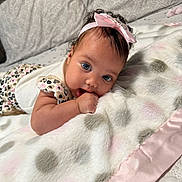 Saniyah joined the competition — help win amazing prizes! baby, child, infant, portrait, face, eyes, smiling, pink_bow, headband, curly_hair, lying_down, blanket, fluffy_blanket, bed, bedding, home, indoors, closeup, baby_clothing, cozy