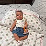 baby, infant, child, portrait, lying_down, bed, blanket, pillow, bow_headband, smiling, face, denim_skirt, sneakers, purse, bedroom, dresser, indoor, fashion, polka_dots, photography