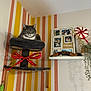 cat, cat_tree, ribbon, striped_wall, yellow, peach, photo_frame, memories, peppermint_candy, decor, shelf, plant, toy_mouse, indoor, furniture, pet, gray_cat, white_cat, cozy, relaxed