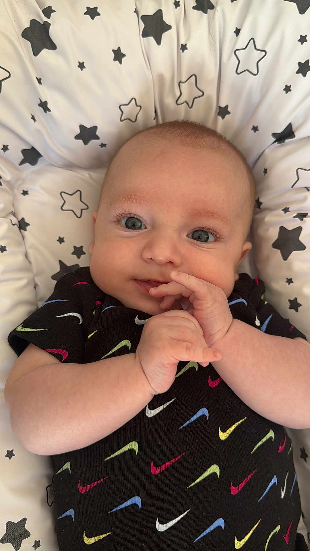 Sonny a rejoint le concours — aidez-le/la à gagner de superbes lots ! baby, infant, face, hands, smile, eyes, clothing, pattern, stars, cushion, comfort, cute, portrait, black_shirt, colorful, swoosh, lying_down, expression, young_child, indoors