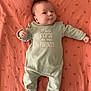 baby, infant, onesie, bedspread, fabric, pattern, lying_down, smile, face, hair, mint_green, coral, text_on_clothing, cute, child, person, sleepwear, soft_texture, indoors, portrait