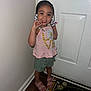 Miliani Rose is registered to the contest to win money with this photo: child, girl, smiling, standing, indoor, door, pink_top, green_shorts, pink_sandals, beaded_hair, floor_mat, white_wall, wooden_floor, happy, cute, portrait, casual_clothing, young_child, playful, person