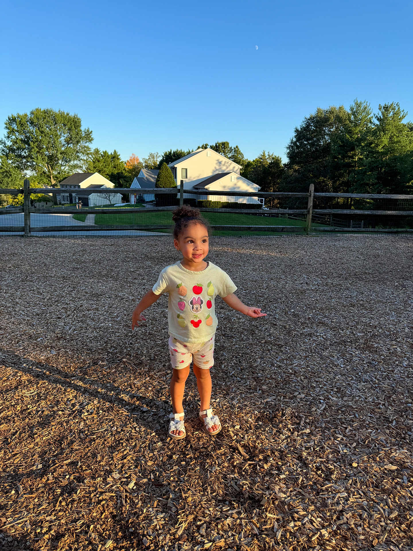 Miliani Rose joined the competition — help win amazing prizes! child, girl, playground, woodchips, tshirt, shorts, sandals, sunlight, shadow, smile, outdoor, daytime, suburban, house, fence, trees, blue_sky, person, cute, happy