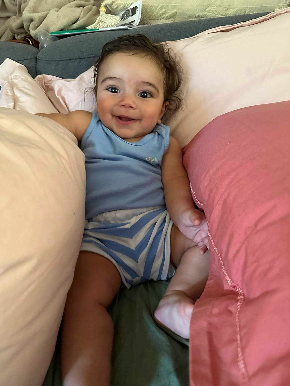 Ahmed a rejoint le concours — aidez-le/la à gagner de superbes lots ! baby, smiling, child, indoors, couch, pillows, happy, face, person, blue_clothing, striped_shorts, cute, skin, hair, infant, relaxed, comfort, living_room, soft, seated