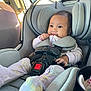 baby, car_seat, child, infant, safety_harness, clothing, pajamas, seatbelt, car_interior, smile, face, cute, young_child, soft_lighting, window, seat, baby_clothes, hands, footwear, car