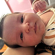 Lorena is registered to the contest to win money with this photo: baby, infant, face, close_up, eyes, nose, mouth, cheeks, hair, onesie, clothing, hand, arm, lying_down, indoor, soft_lighting, portrait, pink_background, cute, newborn