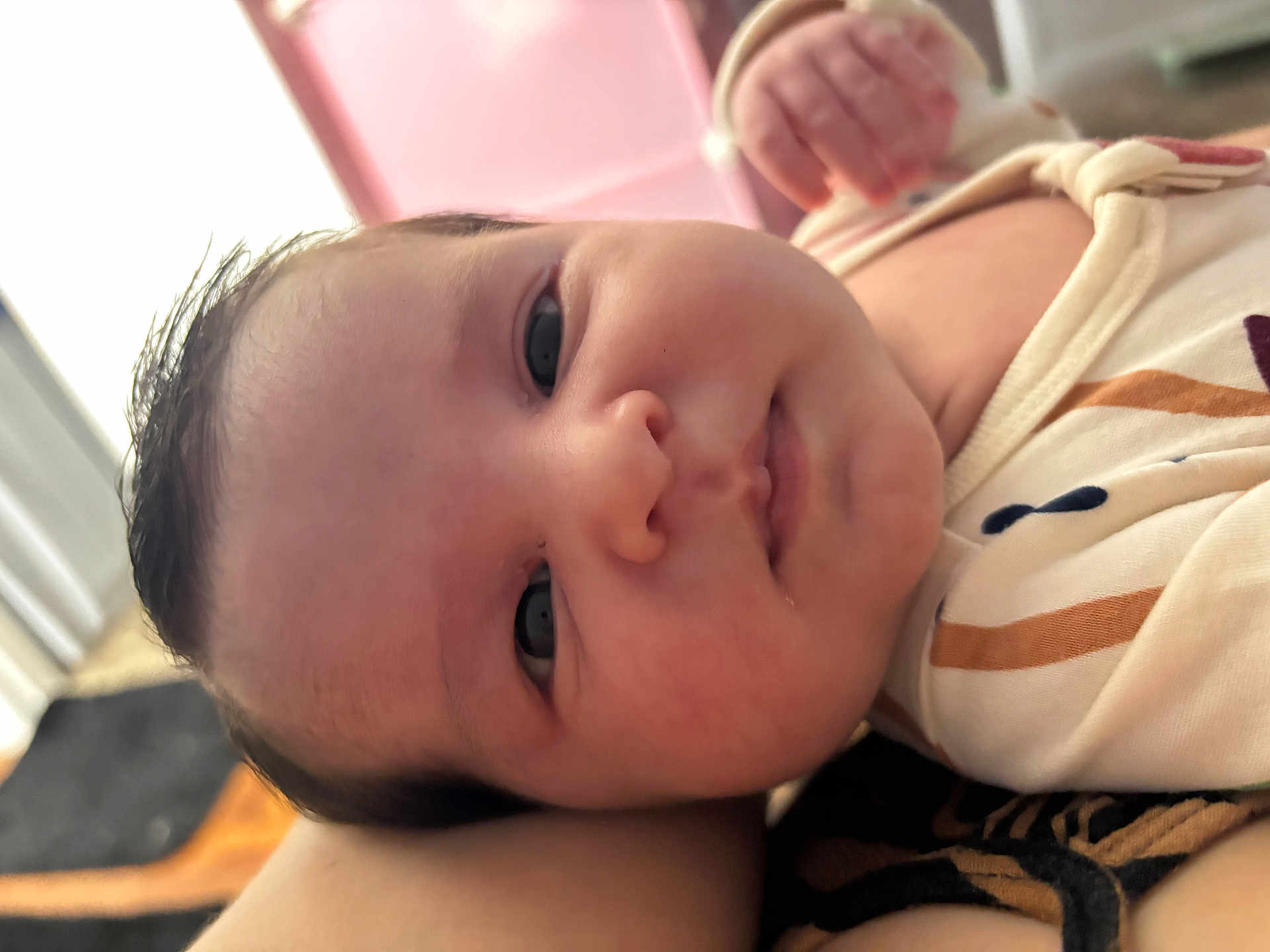 Lorena is registered to the contest to win money with this photo: baby, infant, face, close_up, eyes, nose, mouth, cheeks, hair, onesie, clothing, hand, arm, lying_down, indoor, soft_lighting, portrait, pink_background, cute, newborn