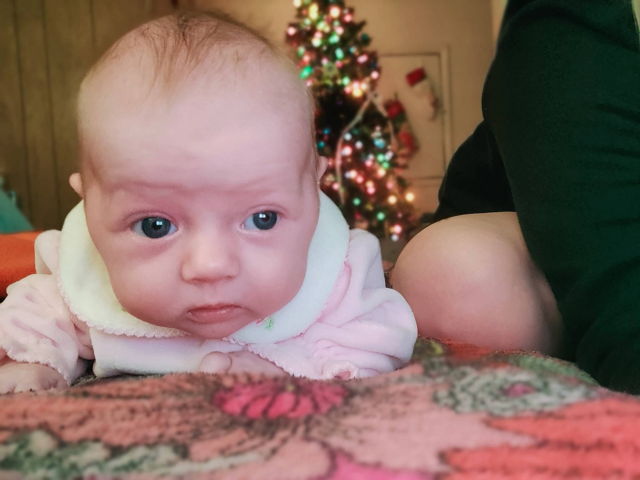 Emersynn is registered to the contest to win money with this photo: baby, baby_toddler_clothing, cheek, child, christmas_tree, comfort, event, eye, fun, happy, holiday, iris, linens, person, room, sitting, skin, toddler, tree, tummy_time