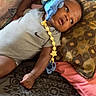 Amari is registered to the contest to win money with this photo: baby, infant, child, onesie, nike, plush_toy, bed, pillow, patterned_bedspread, looking_away, curious, indoor, resting, cute, small_child, colorful, soft_toy, lying_down, relaxed, casual_clothing