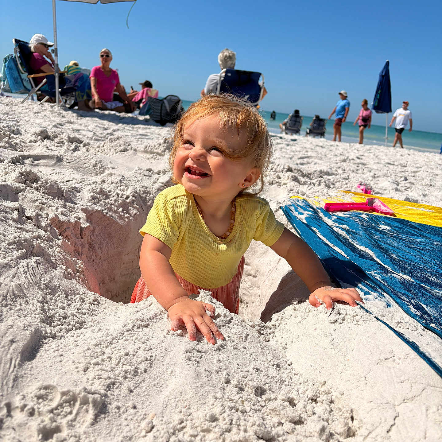 Maylynn is registered to the contest to win money with this photo: toddler, child, beach, sand, sunny, umbrella, smiling, yellow_shirt, playing, hole, happy, outdoor, vacation, summer, people, ocean, sky, relaxation, family, fun