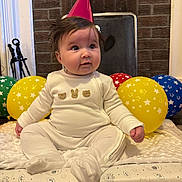 Frankie is registered to the contest to win money with this photo: baby, party_hat, balloons, indoor, carpet, blanket, cushion, cute, child, white_clothing, celebration, birthday, infant, plush, face, sitting, floor, headwear, smiling, decor