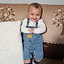 baby, child, smiling, denim_overalls, couch, cushion, white_pillow, indoor, happy, cute, face, person, footwear, socks, home, portrait, infant, standing, cozy, fabric