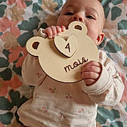 Mia a rejoint le concours — aidez-le/la à gagner de superbes lots ! baby, baby_girl, blanket, cherry_print, child, clothing, cute, face, hand, indoor, infant, lying_down, month_marker, pattern, pink_pants, plaque, portrait, soft_light, wood, wooden_sign