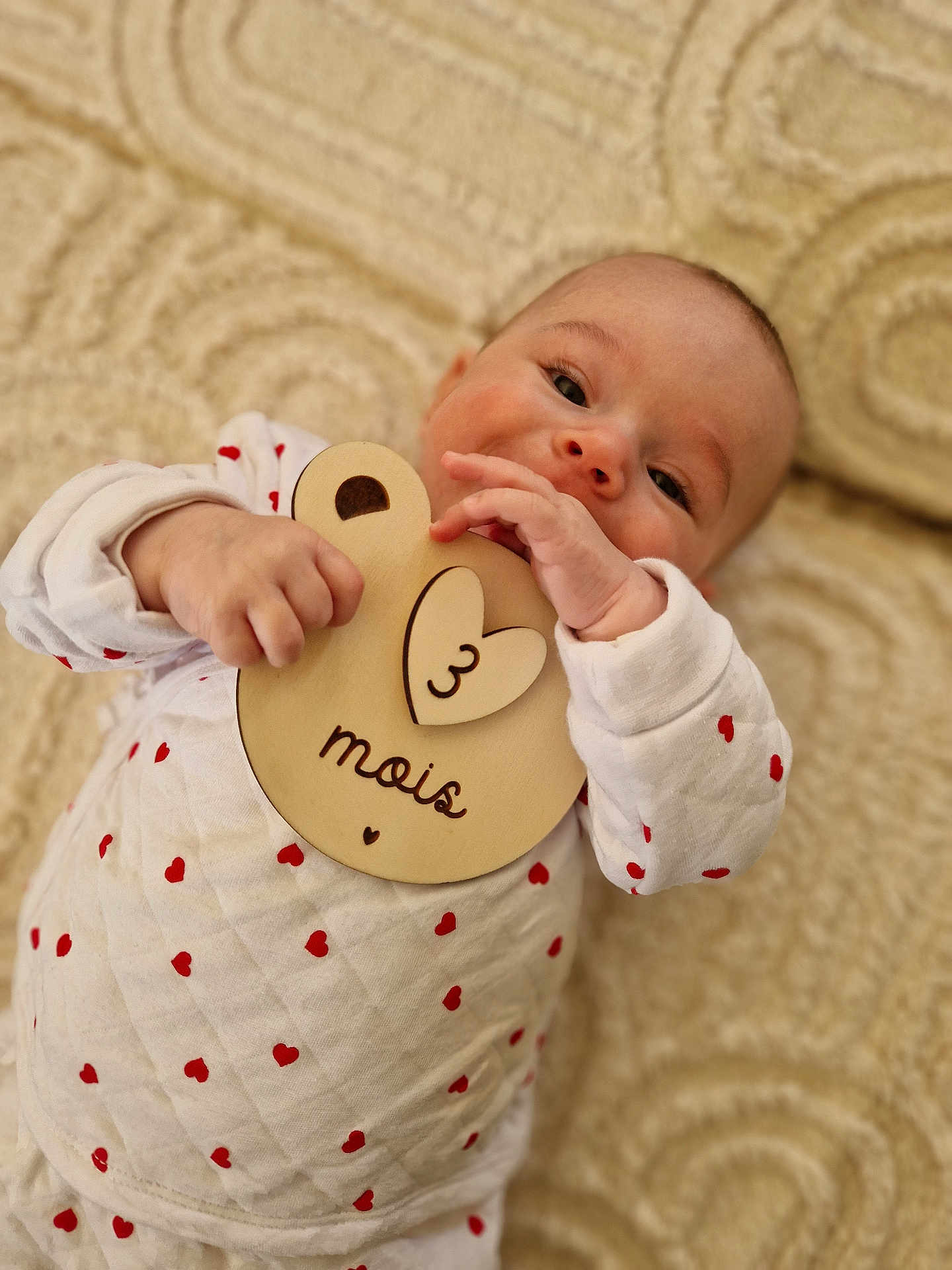 Mia participe au concours pour gagner de l'argent avec cette photo : baby, infant, child, cute, lying_down, white_clothing, red_hearts, wooden_toy, plaque, face, hand, blanket, soft_texture, indoors, portrait, smiling, happy, close_up, person, young