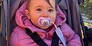 Kelia participe au concours pour gagner de l'argent avec cette photo : baby, infant, stroller, pacifier, pink_jacket, harness, canopy, hand, eyes, portrait, outdoors, sunlight, nature, grass, seat, hood, pacifier_clip, cute, bundle_up, winter_clothing
