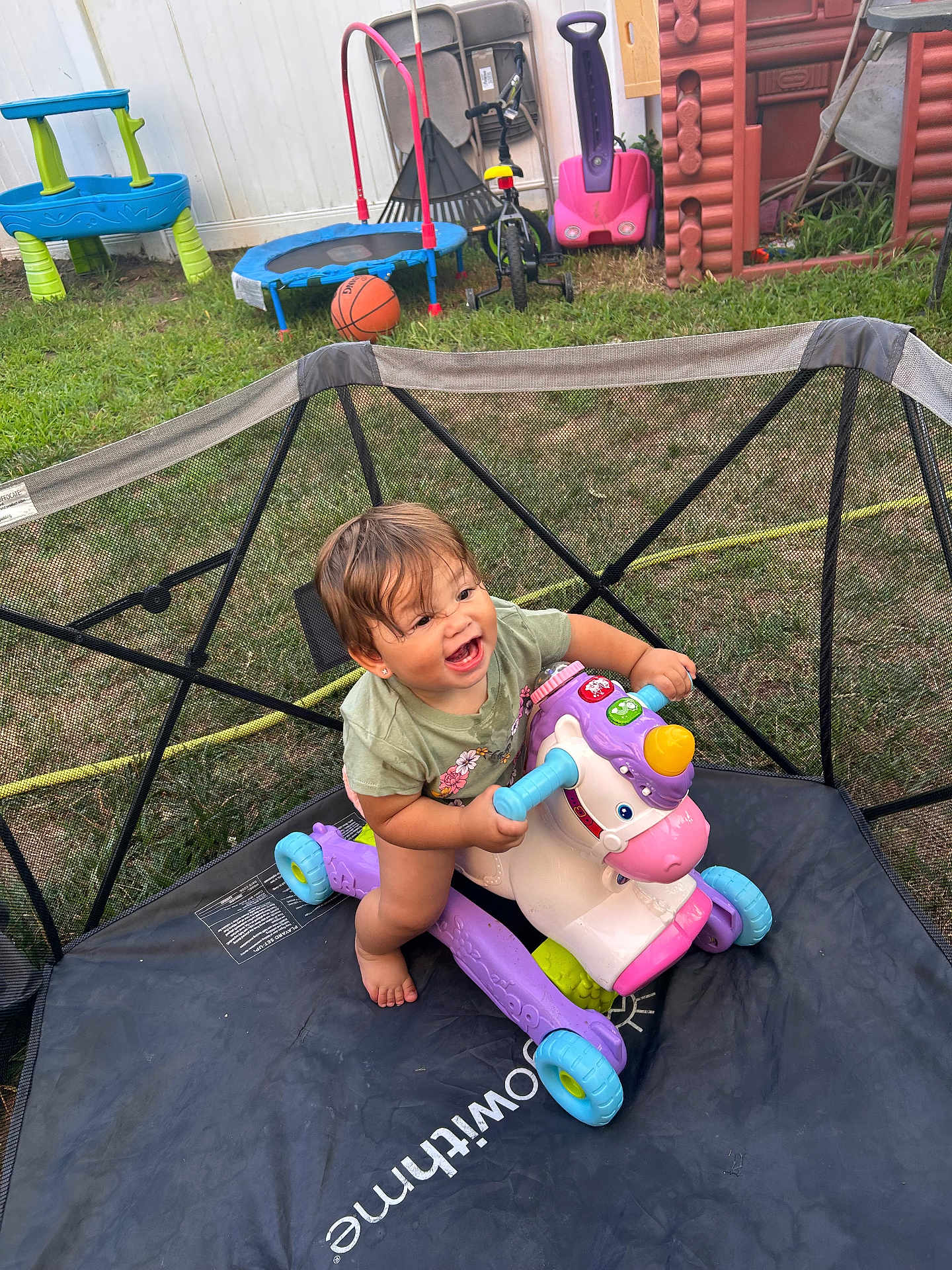 Amaiahkali is registered to the contest to win money with this photo: toddler, toy, unicorn, trampoline, outdoor, grass, playground, basketball, tricycle, slide, child, happy, smiling, barefoot, green_tshirt, plastic_toy, fence, summer, fun, play