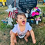 Amaiahkali is registered to the contest to win money with this photo: toddler, child, grass, gravestone, flower, flag, cemetery, smile, happy, outdoor, memorial, headstone, nature, person, portrait, casual_clothing, earrings, sunlight, daytime, greenery