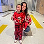 child, baby, woman, indoor, floor, plaid_pants, sweater, red_clothing, polka_dots, pacifier, smile, holding, crouching, happy, person, casual, holiday, patterned_floor, family, together
