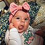 baby, pink_bow, headband, tongue_out, cute, infant, patterned_cushion, clothing, long_sleeve, face, hand, cheek, resting, indoors, portrait, expression, adorable, child, young, smiling