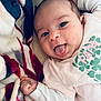 baby, infant, tongue_out, blanket, cozy, cute, playful, clothing, shirt, face, hand, lying_down, expression, indoor, young_child, person, portrait, smiling, soft_texture, colorful