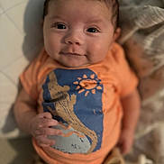 Luca joined the competition — help win amazing prizes! baby, infant, child, face, smile, clothing, orange_shirt, blanket, soft, cute, portrait, young_child, lying_down, hand, expression, indoor, warm_colors, cozy, eyes, skin