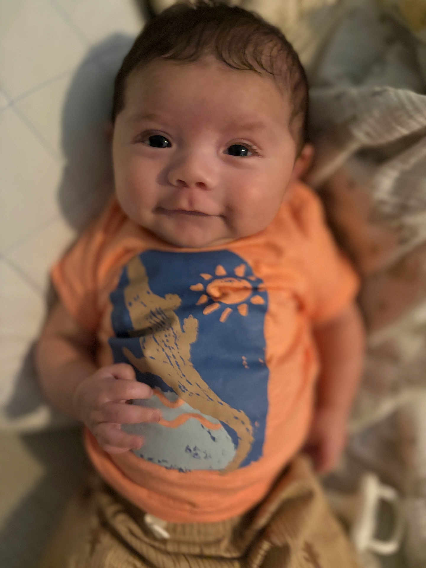 Luca joined the competition — help win amazing prizes! baby, infant, child, face, smile, clothing, orange_shirt, blanket, soft, cute, portrait, young_child, lying_down, hand, expression, indoor, warm_colors, cozy, eyes, skin