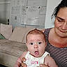 baby, woman, couch, indoor, expression, surprised, holding, striped_clothing, face, person, furniture, home, whiteboard, wall, seated, skin, head, hand, clothing, tattoo