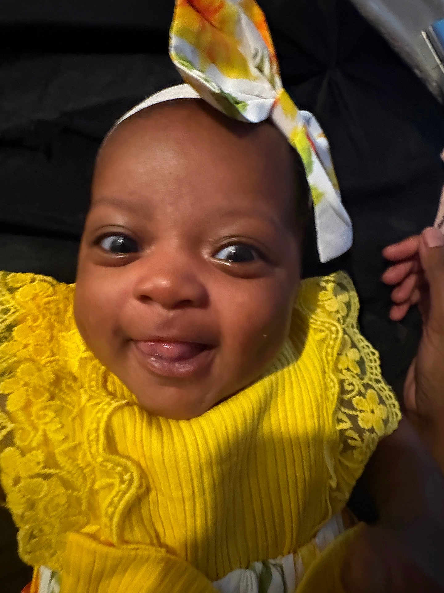 Zuri joined the competition — help win amazing prizes! baby, child, smile, yellow_dress, headband, tongue_out, close_up, portrait, happy, infant, face, hand, clothing, lace, bright_colors, cute, young_child, indoor, person, dark_background