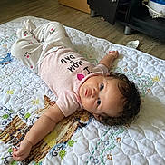 Journi joined the competition — help win amazing prizes! baby, blue_eyes, cabinet, child, clothing, curly_hair, cute, expression, floor, furniture, home, indoor, infant, lying_down, person, pink_shirt, quilt, stroller_wheel, toddler, white_pants