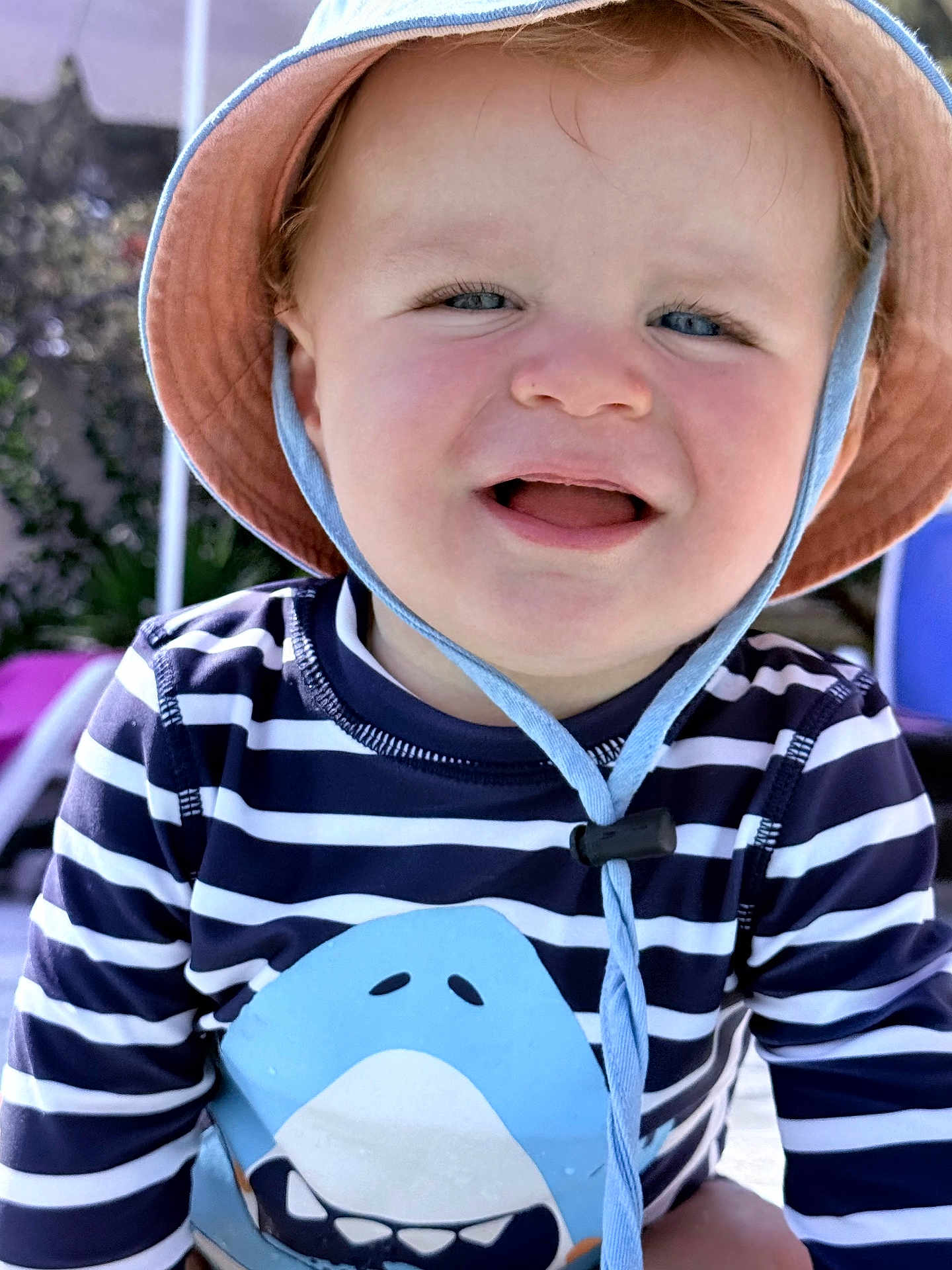 Louis a rejoint le concours — aidez-le/la à gagner de superbes lots ! toddler, child, smiling, hat, striped_shirt, shark_graphic, outdoor, sunlight, blue_eyes, happy, cute, baby, face, clothing, summer, playful, portrait, fun, person, headwear