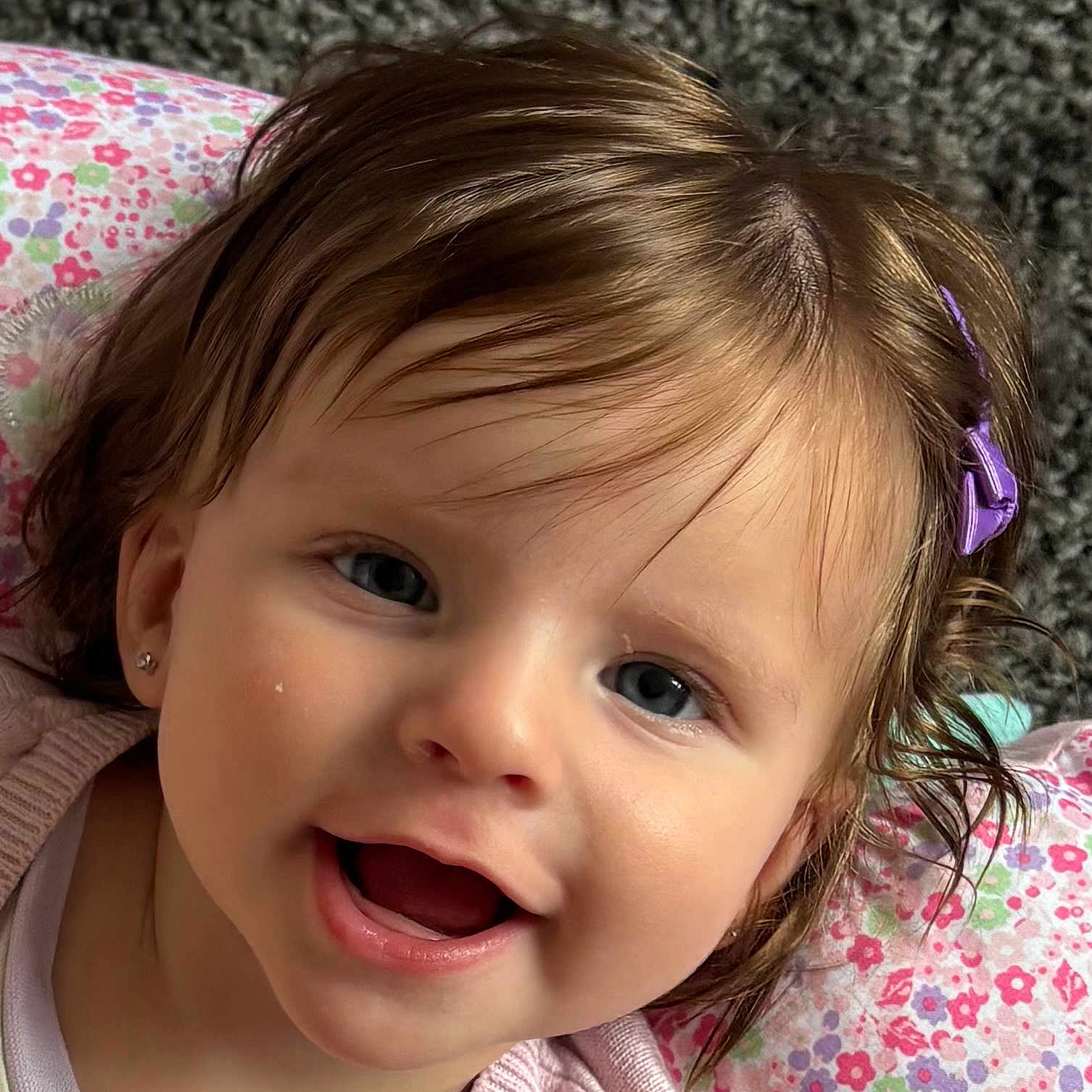 Callie-Anne joined the competition — help win amazing prizes! baby, blue_eyes, child, close_up, cute, earrings, expression, face, floral_pillow, hair_clip, happy, head, indoors, infant, person, pink_clothing, portrait, skin, smile, young