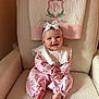 baby, infant, headband, bow, pink_outfit, tulip_pattern, quilted_towel, armchair, nursery_chair, smile, rosy_cheeks, sitting, bare_feet, hands_clasped, portrait, soft_texture, embroidered_monogram, pink_color_palette, cozy, adorable