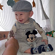 Owen participe au concours pour gagner de l'argent avec cette photo : baby, child, smiling, cap, overalls, mickey_mouse, plush_toy, hand, mobile, stars, clouds, curtain, pattern, white_surface, socks, happy, indoor, person, cute, supporting_hand