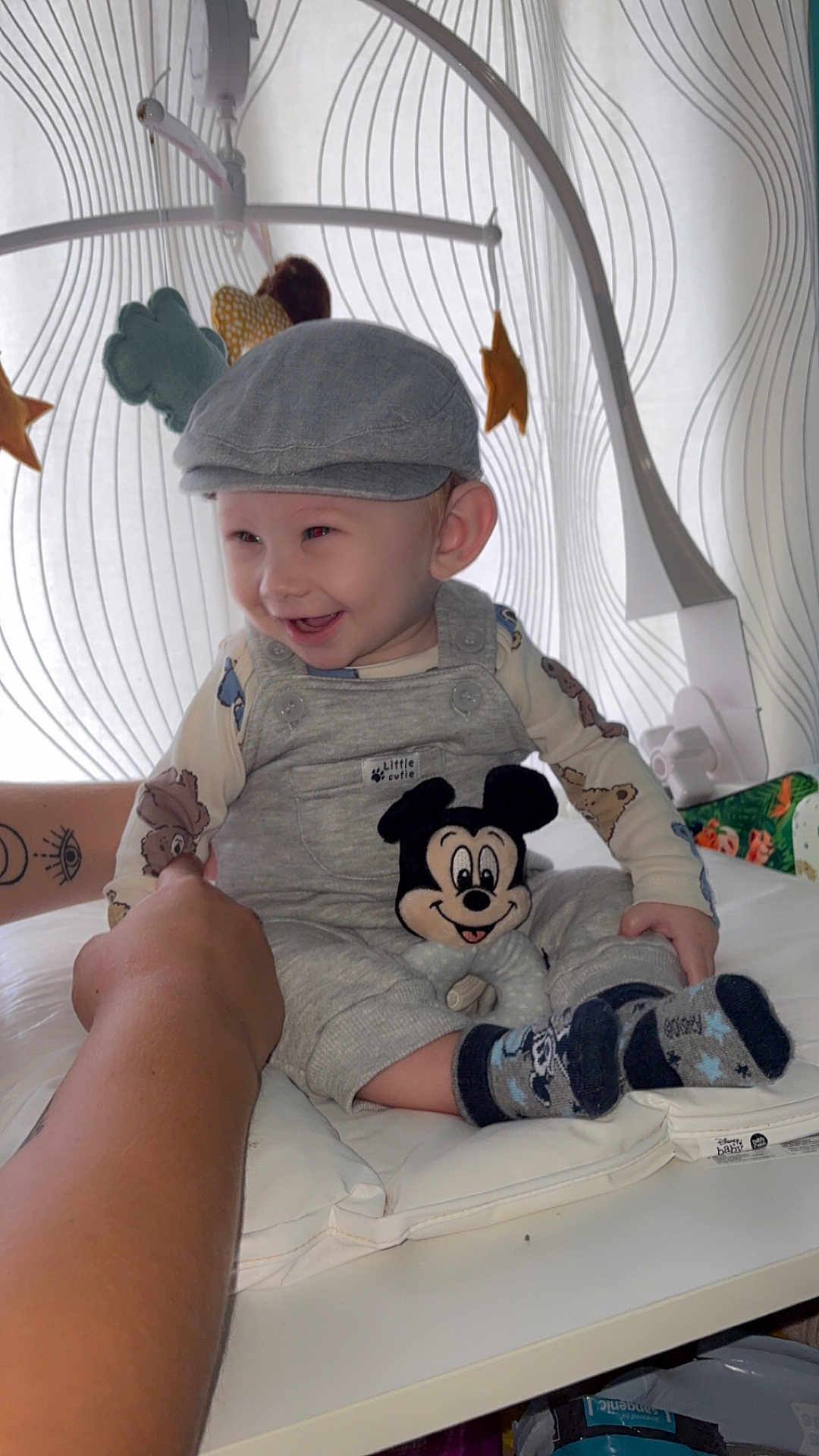 Owen participe au concours pour gagner de l'argent avec cette photo : baby, child, smiling, cap, overalls, mickey_mouse, plush_toy, hand, mobile, stars, clouds, curtain, pattern, white_surface, socks, happy, indoor, person, cute, supporting_hand