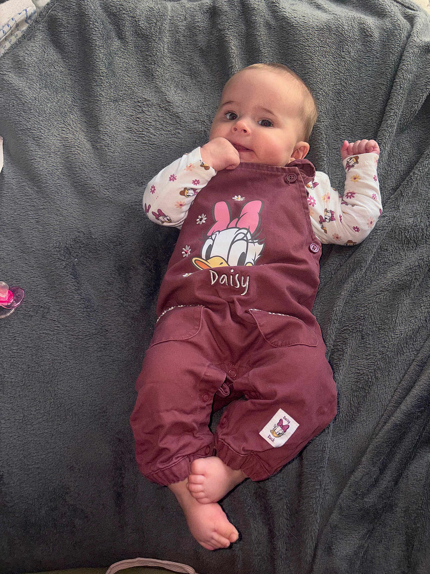 Célina -Marie a rejoint le concours — aidez-le/la à gagner de superbes lots ! baby, child, infant, face, hands, feet, clothing, overalls, daisy_duck, blanket, lying_down, cute, expression, soft_texture, maroon, cartoon_character, sleeves, patterned, indoor, portrait
