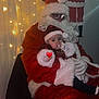 baby, child, santa_claus, christmas, holiday, festive, lights, costume, beard, glasses, red_clothing, white_fur, indoor, decorations, person, seated, thumb_sucking, heart_emoji, wall_art, chair