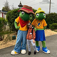 Kenzo a rejoint le concours — aidez-le/la à gagner de superbes lots ! child, mascot, costume, turtle, outdoor, pavement, greenery, cap, jacket, glasses, smile, person, fun, character, feet, pants, trees, overcast, nature, friendship