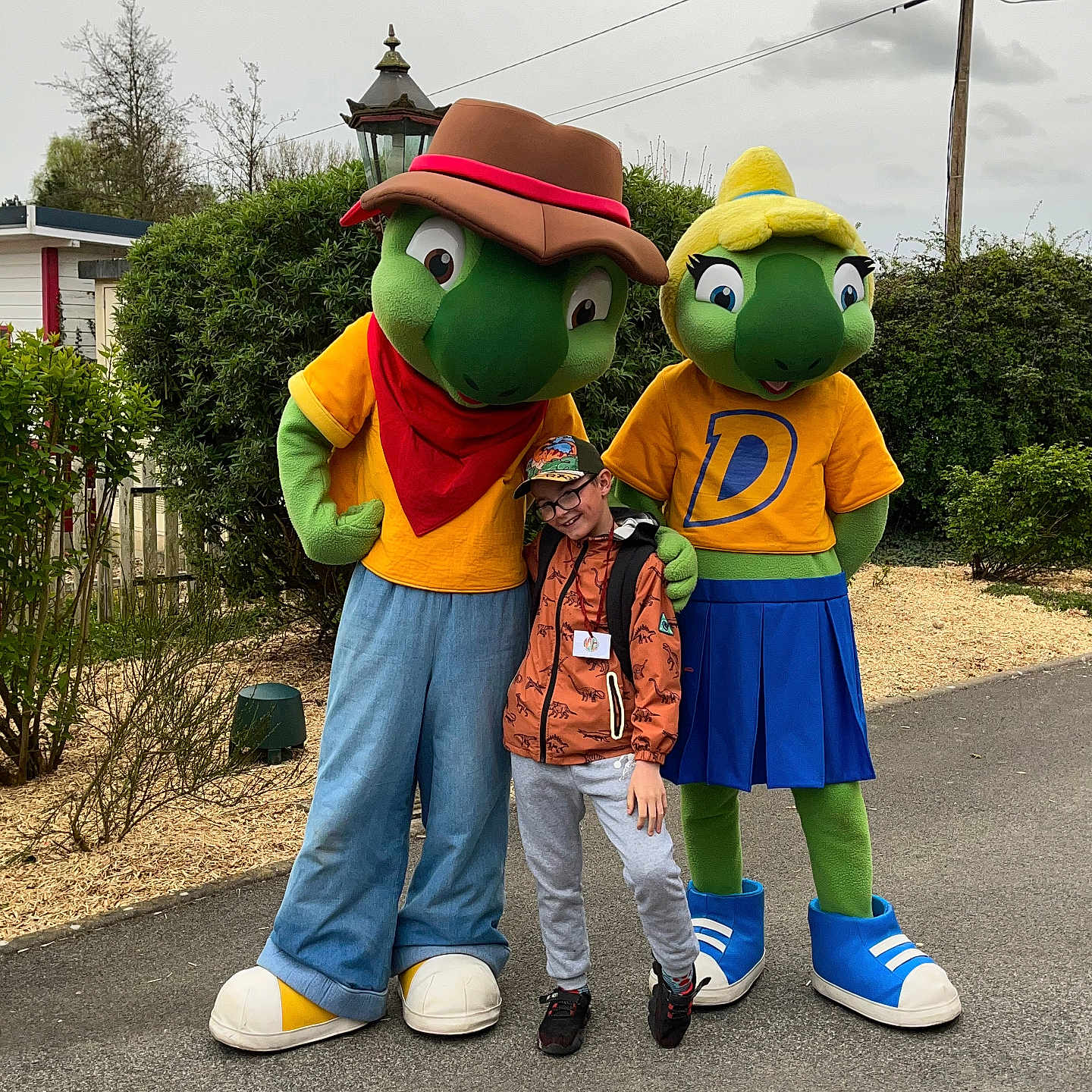 Kenzo a rejoint le concours — aidez-le/la à gagner de superbes lots ! cap, character, child, costume, feet, friendship, fun, glasses, greenery, jacket, mascot, nature, outdoor, overcast, pants, pavement, person, smile, trees, turtle