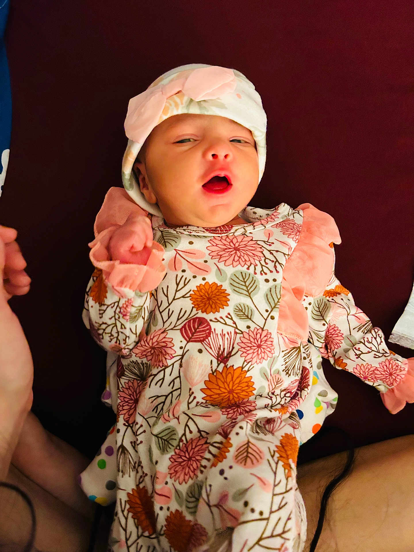 Mirha joined the competition — help win amazing prizes! baby, infant, child, hat, bow, floral_pattern, clothing, hand, lying_down, face, person, cute, newborn, pink, orange, white, background, soft, expression, warm