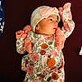 baby, infant, child, floral_clothing, hat, pink, orange, ruffles, lying_down, maroon_background, newborn, cute, portrait, small_hands, face, clothing, apparel, headwear, looking_sideways, soft_lighting