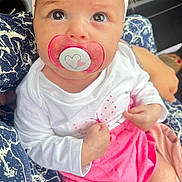 Inaya a rejoint le concours — aidez-le/la à gagner de superbes lots ! baby, pacifier, headband, white_clothing, pink_skirt, infant, person, closeup, car_interior, seated, hand, patterned_fabric, cute, child, portrait, young, skin, eyes, expression, holding