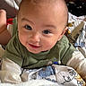baby, bed, blanket, child, cozy, cute, expression, eyes, face, green_shirt, happy, head, indoor, infant, lying_down, person, portrait, skin, smile, young