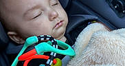 Kylan is registered to the contest to win money with this photo: baby, sleeping, car_seat, toy, blanket, hand, infant, child, colorful, cozy, peaceful, closeup, indoor, soft_lighting, portrait, cute, rest, comfort, seatbelt, fabric