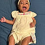 Aaliyah is registered to the contest to win money with this photo: apparel, arms, baby, blue_background, child, clothing, cream_color, cute, floral_embroidery, happy, headband, indoors, infant, legs, lying_down, mouth_open, person, playful, skin, smiling