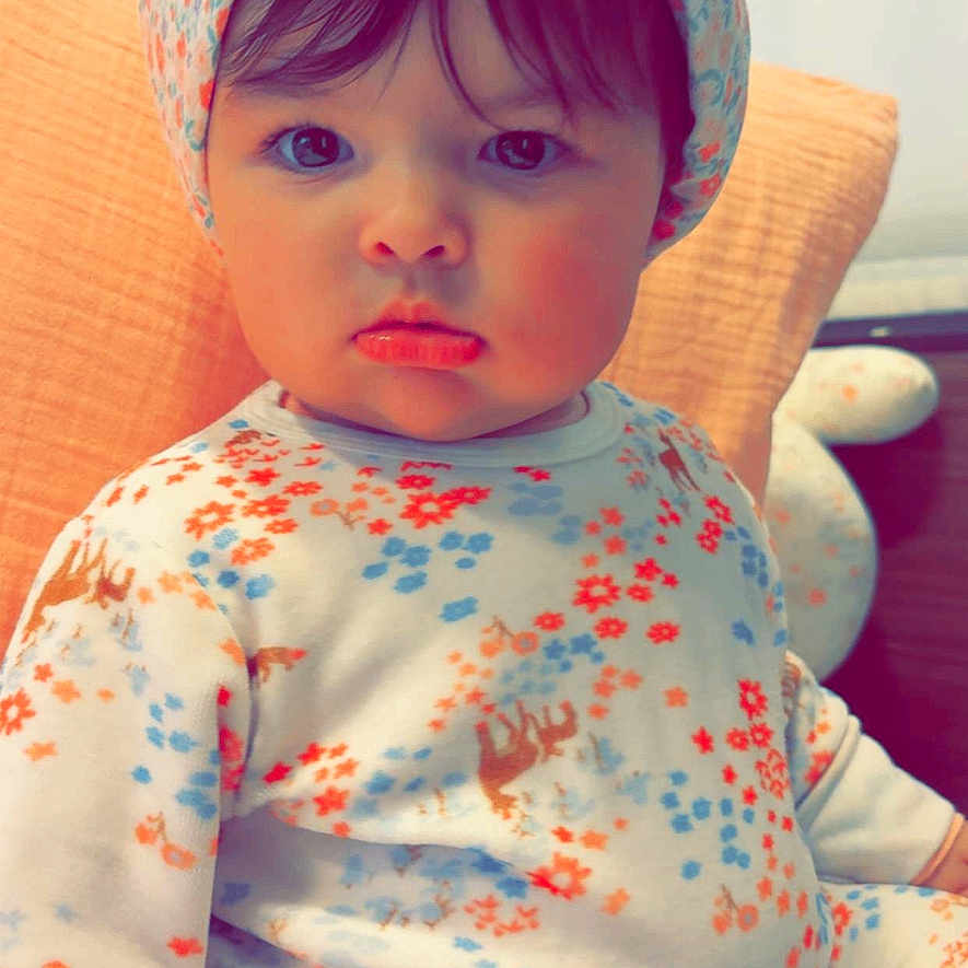 Bianca participe au concours pour gagner de l'argent avec cette photo : baby, child, pajamas, head_wrap, floral_pattern, indoor, pillow, seated, cute, portrait, face, expression, clothing, soft_lighting, home, young_child, person, infant, headwear, sitting