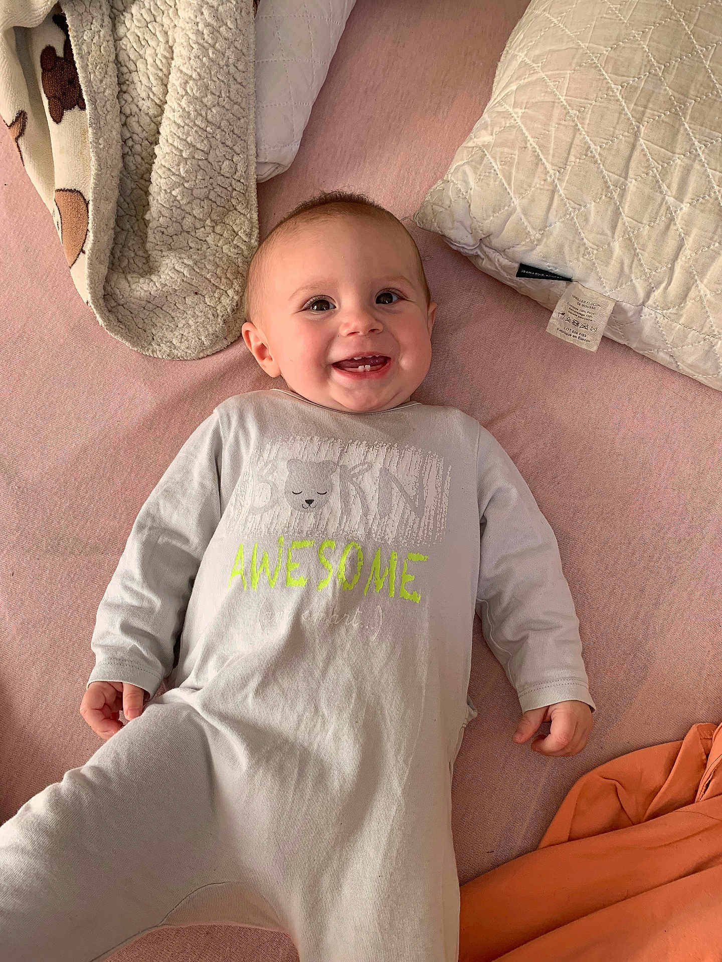 Thalya participe au concours pour gagner de l'argent avec cette photo : baby, smile, happy, onesie, infant, bed, pillow, blanket, pink, clothing, child, cute, lying_down, indoors, face, young_child, cozy, soft, relaxed, teeth
