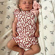 Thalya participe au concours pour gagner de l'argent avec cette photo : baby, sleeping, romper, red_flowers, stuffed_toy, pink_toy, blanket, soft_texture, infant, peaceful, resting, cute, child, patterned_blanket, lying_down, closed_eyes, small_hands, small_feet, indoors, cozy