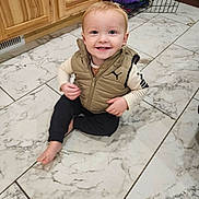 Aiden joined the competition — help win amazing prizes! toddler, child, smiling, sitting, indoor, kitchen, floor, tile, marble, wooden_cabinets, pet_crate, clothing, vest, shirt, pants, barefoot, portrait, happy, face, photography