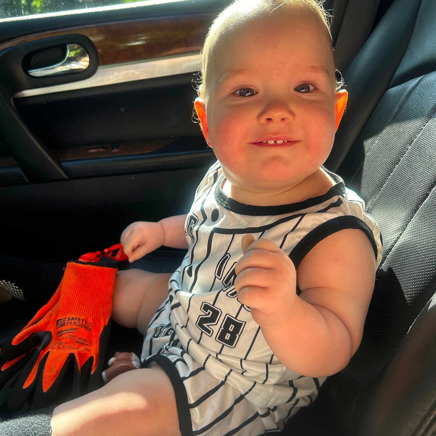 Waylon is registered to the contest to win money with this photo: baby, black_seat, car_interior, car_seat, child, clothing, cute, daylight, face, hand, indoor, leg, number_28, orange_gloves, person, seat, smile, striped_outfit, sunlight, window