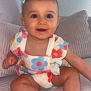 Eyna participe au concours pour gagner de l'argent avec cette photo : baby, child, cute, smiling, blue_bow, floral_outfit, sitting, couch, cozy, indoor, portrait, happy, infant, skin, face, eyes, hand, legs, furniture, home